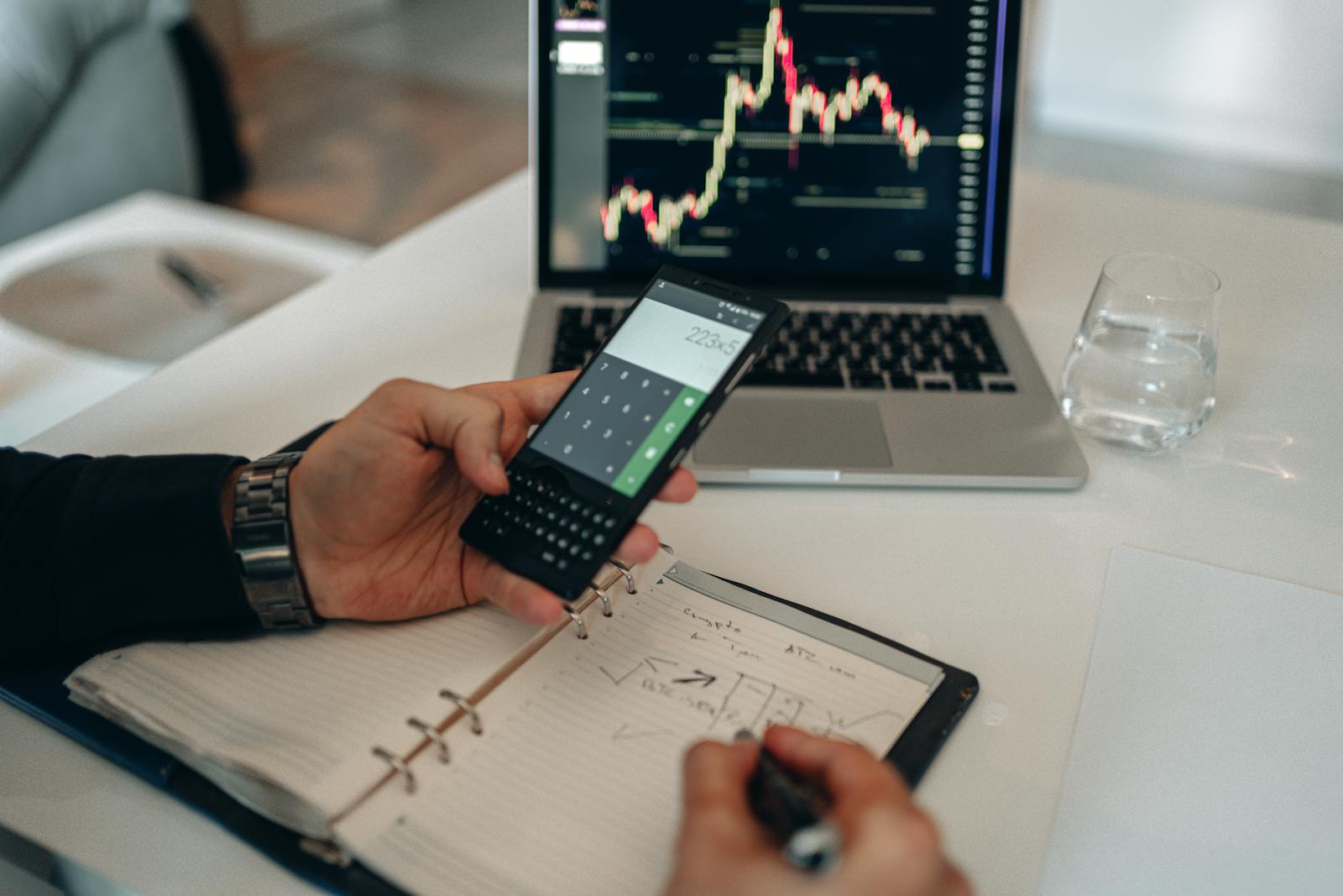 Expense records being calculated on a phone beside a notebook and laptop